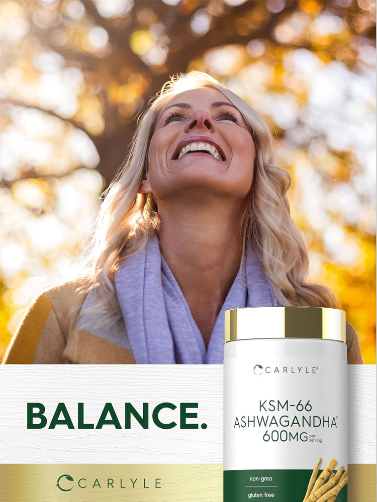 A middle-aged blonde woman smiling outdoors near autumn leaves and a Carlyle KSM-66 Ashwagandha bottle.