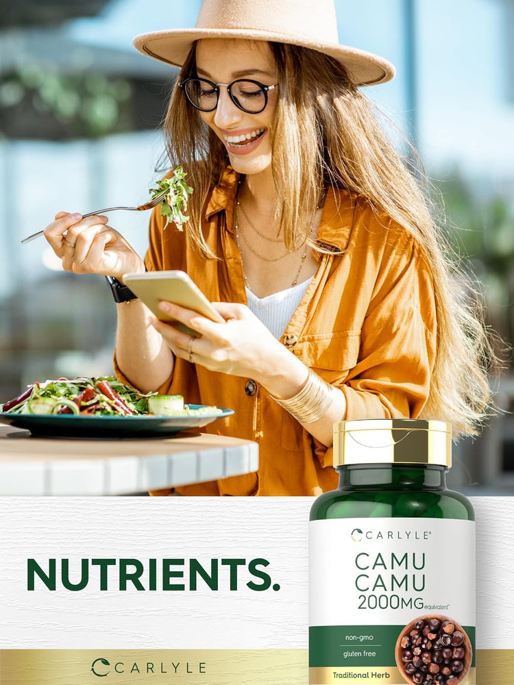 Young woman eats a salad while looking at her phone, next to a Carlyle Camu Camu 2000MG Equivalent bottle.