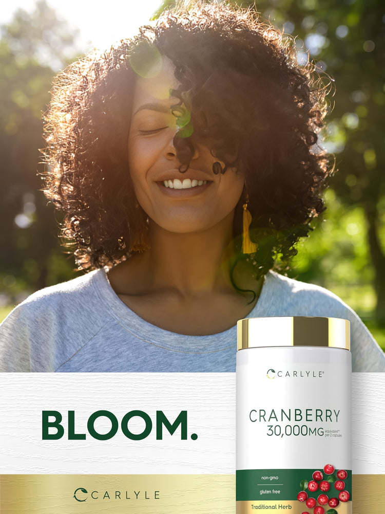 An adult woman smiles with eyes closed in sunlight, next to a Carlyle Cranberry 30,000mg supplement bottle.