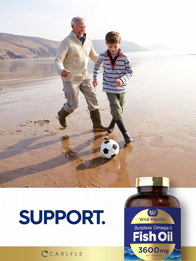 An older man and young boy play soccer on a beach, featuring a bottle of Carlyle Fish Oil nearby.