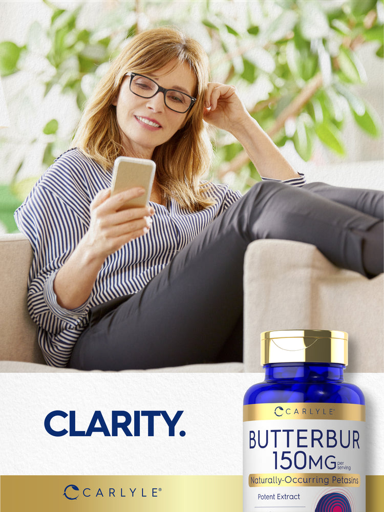 Middle-aged woman smiling at her phone on a couch, next to a Butterbur bottle.