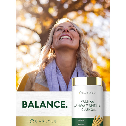 View 6 A middle-aged blonde woman smiling outdoors near autumn leaves and a Carlyle KSM-66 Ashwagandha bottle.