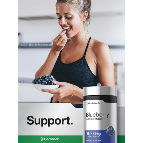 View 6 Young adult woman in sportswear smiling while eating a blueberry from a bowl, with a Horbäach Blueberry Concentrate bottle.