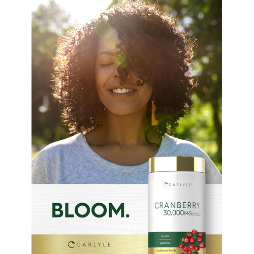 View 6 An adult woman smiles with eyes closed in sunlight, next to a Carlyle Cranberry 30,000mg supplement bottle.