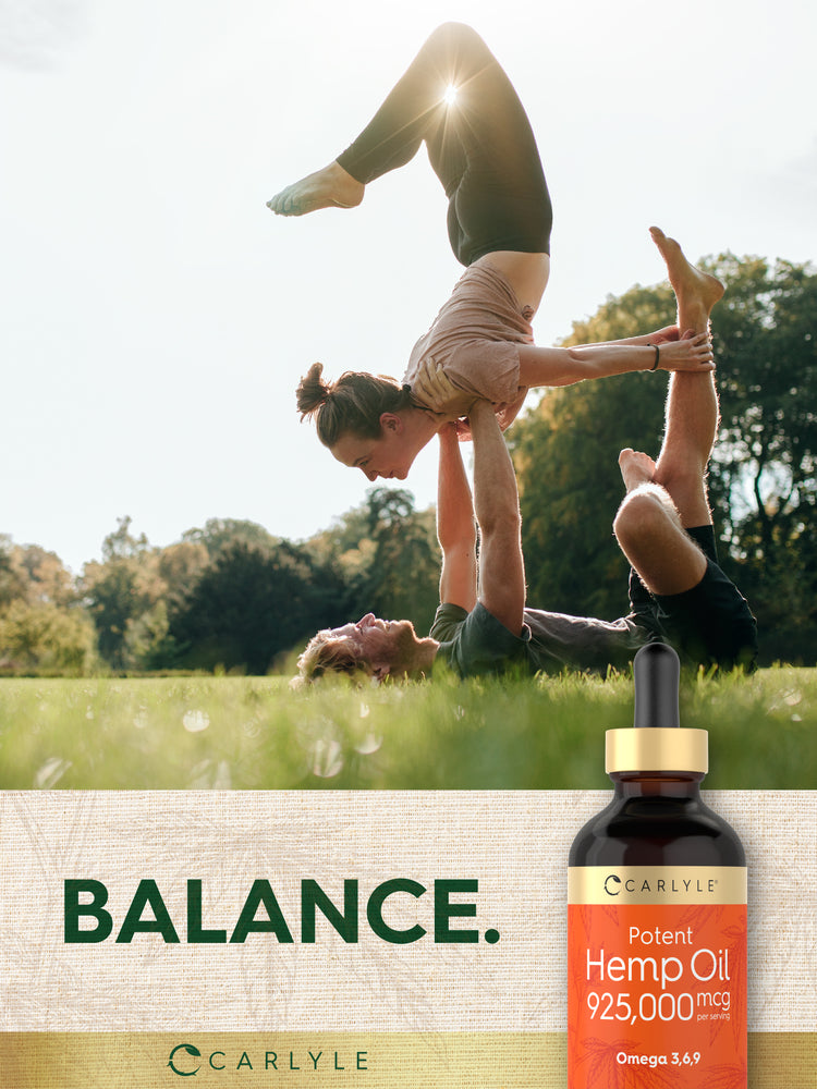 Two young adults perform an acroyoga pose in a sunny park with a Carlyle Potent Hemp Oil bottle.