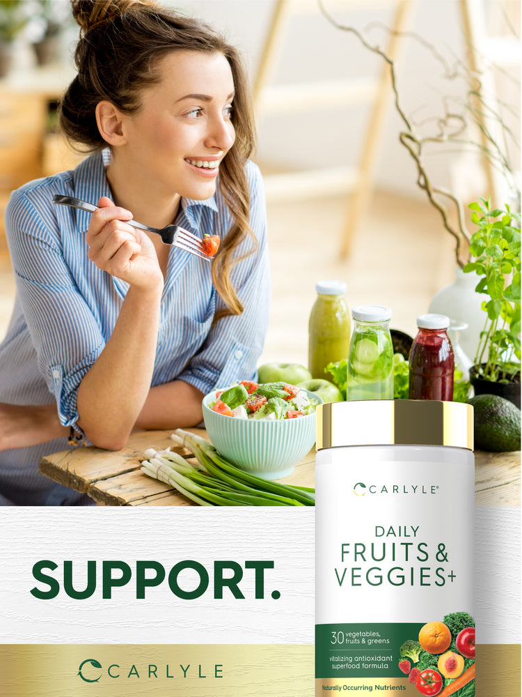 A woman enjoys a salad at a wooden table with healthy foods, next to a Daily Fruit & Veggies bottle.