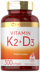 Carlyle Vitamin K2 + D3 supplement with 300 softgels, shown on a hand scale, indicating its bulk size.
